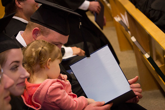 A graduate sits down with his little girl during Convocation to show her his diploma.