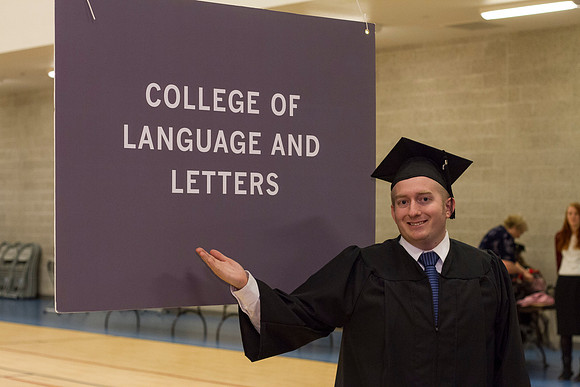 A graduate smiles in front of the College of Language and Letters sign in the I-Center.