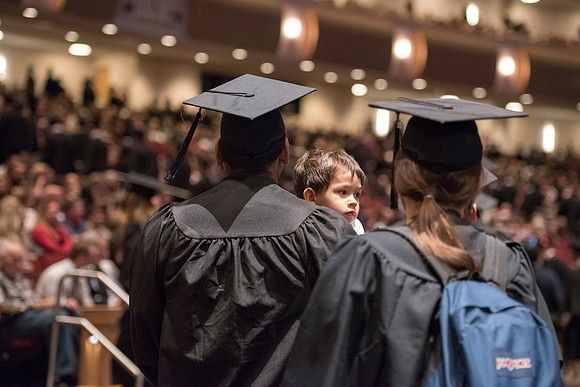 A graduates carries his child during recessional. Photo by Ryan Chase