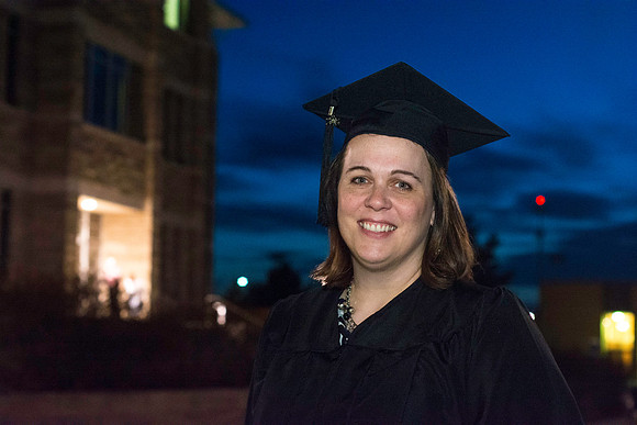 An Interdisciplinary Studies graduate stands outside the Kirkham Building after convocation. The Jacob Spori Building is in the background.