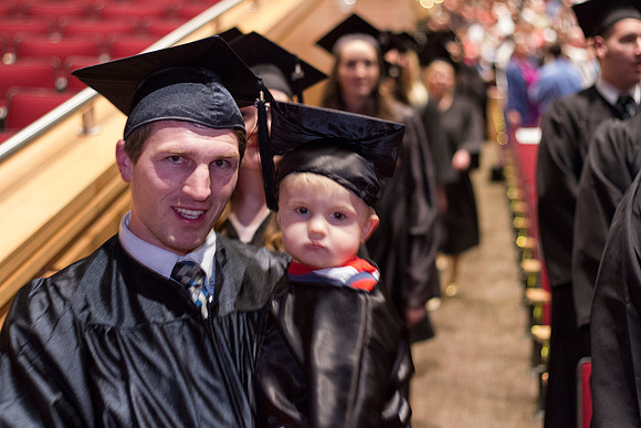 A Winter 2014 graduate smiles as he walks by with his son during the Commencement Ceremony in the the i-Center.