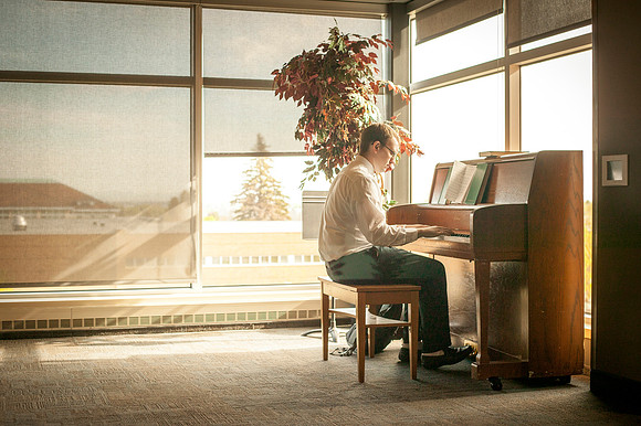 Andy Black practices piano in the Manwaring Center, as soft window light shines down upon him.