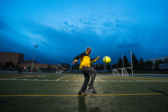 A fan watching the rec soccer game juggles a soccer ball on the sidelines.
