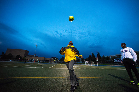 A fan watching the rec soccer game juggles a soccer ball on the sidelines.