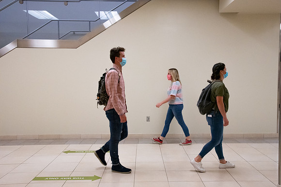 Examples of students staying safe and healthy during the COVID-19 pandemic by social distancing, following pathway arrows, and wearing face masks.