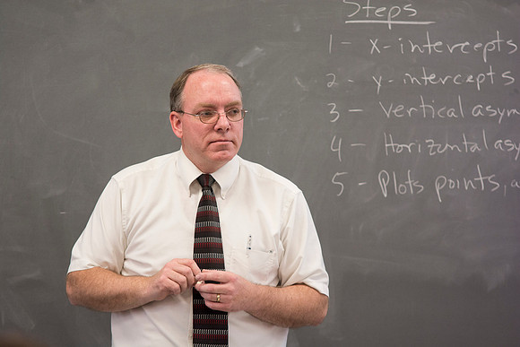 Brother Johanson listens to a student discuss on problem on the board in his Math 109 Precalculus class.