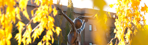 Autumn campus shot of the statue in front of the Austin Building.