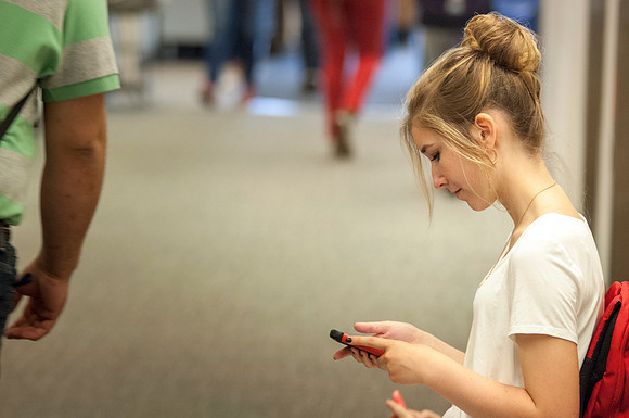 A student sends a quick text as she waits outside her class in the Ricks Building.