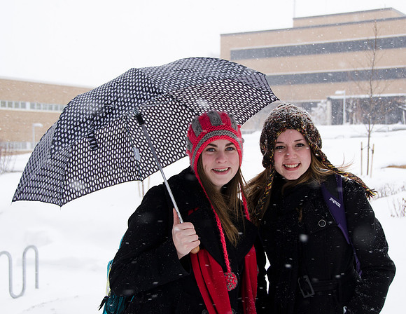 students bundle under an umbrella outside the McKay Library.