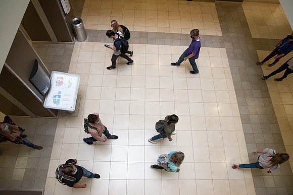 Examples of students staying safe and healthy during the COVID-19 pandemic by social distancing, following pathway arrows, and wearing face masks.