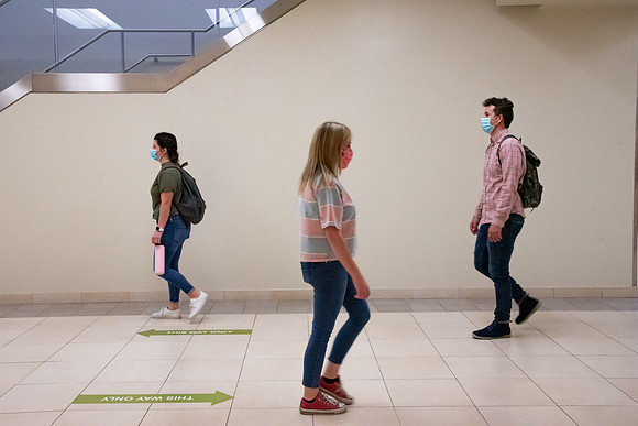 Examples of students staying safe and healthy during the COVID-19 pandemic by social distancing, following pathway arrows, and wearing face masks.