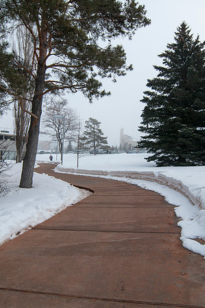 A student walks along the path leading to the Rigby Building.