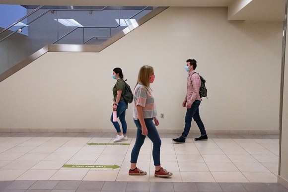 Examples of students staying safe and healthy during the COVID-19 pandemic by social distancing, following pathway arrows, and wearing face masks.