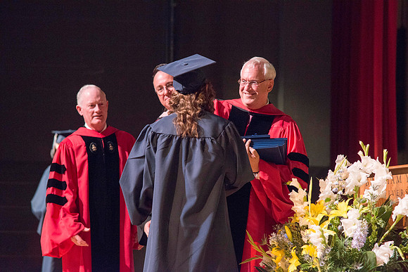 Elder Robert C. Gay of the First Quorum of the Seventy along with President Kim B. Clark and Jon Linford, Dean of the College of Foundations and Interdisciplinary Studies, present the graduates with t