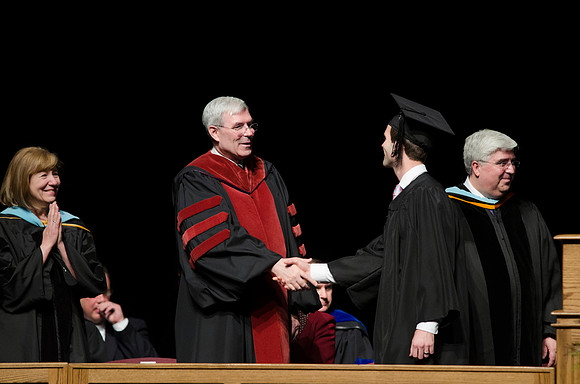 Edwin A. Sexton shakes hands with a graduate from the College of Business and Communication in the Hart Auditorium during Convocation.