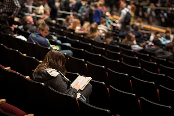A student reads a book before devotional starts.