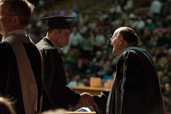 Elder Cook shakes hands with Derrick Hope in the Hart Gym during convocation.