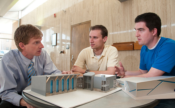 Architecture Construction instructor Dave Barker discusses model design with Jared Bauch(yellow) and Blake McBride in blue.