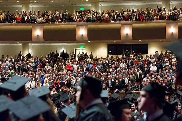 Family and friends of the graduates stand as graduates acknowledge them by applause. Photo by Courtney Thomas.