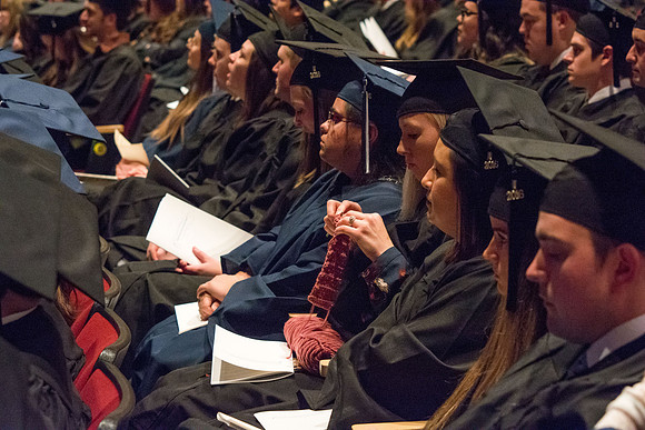 A graduate knits at the Commencement ceremony to pass the time.