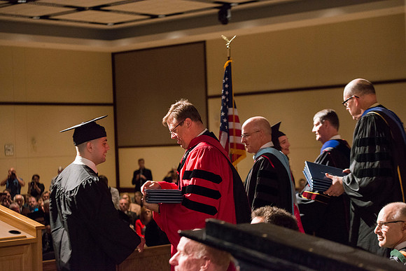 College of Language and Letters Convocation in the Manwaring Center Ballroom. Eric Walz, Pres Gilbert and Elder Clayton present the graduates with their diploma covers.