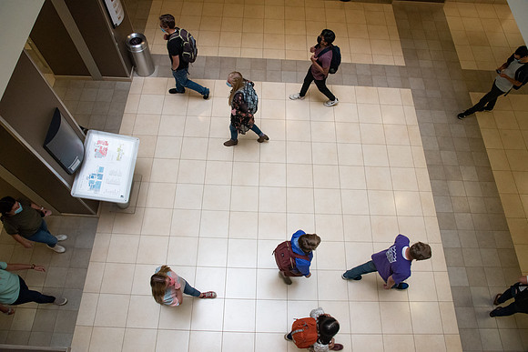 Examples of students staying safe and healthy during the COVID-19 pandemic by social distancing, following pathway arrows, and wearing face masks.
