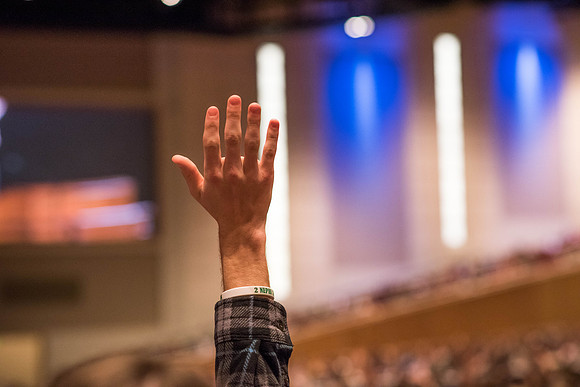 A student raises his hand at Devotional in response to the speaker's question.