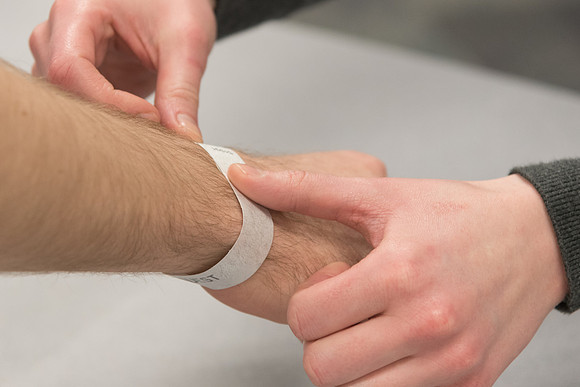An equipment room employee places a wristband on another student.