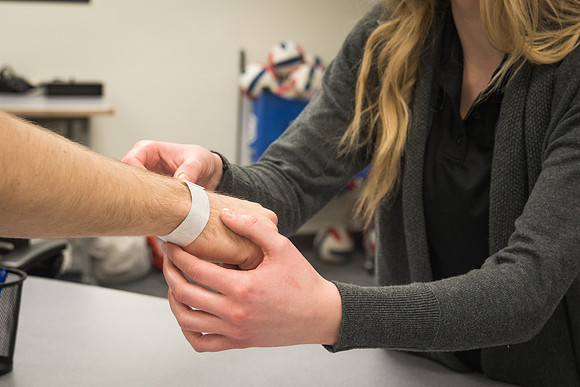 An equipment room employee places a wristband on another student.