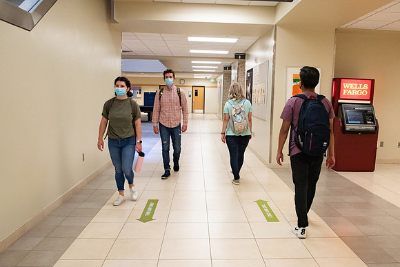 Examples of students staying safe and healthy during the COVID-19 pandemic by social distancing, following pathway arrows, and wearing face masks.