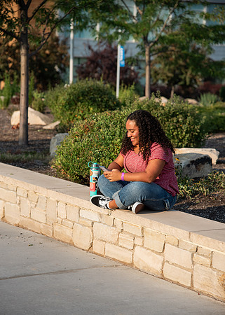 Student on her phone on campus between the Taylor and Manwaring Center.