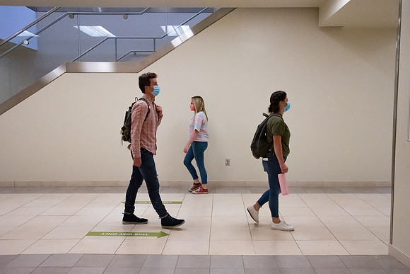 Examples of students staying safe and healthy during the COVID-19 pandemic by social distancing, following pathway arrows, and wearing face masks.