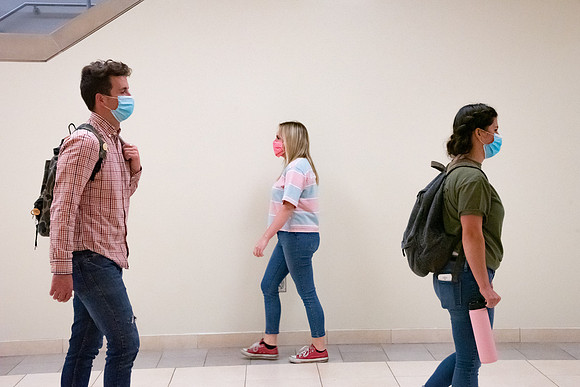 Examples of students staying safe and healthy during the COVID-19 pandemic by social distancing, following pathway arrows, and wearing face masks.