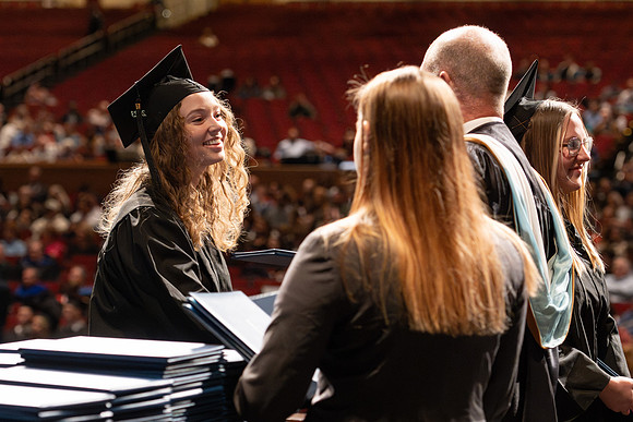 Graduates walk across the stage and accept their diploma.
