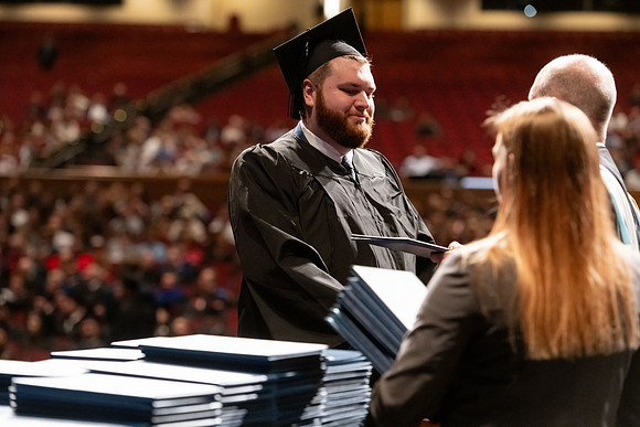 Graduates walk across the stage and accept their diploma.