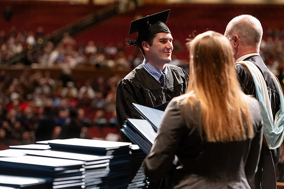 Graduates walk across the stage and accept their diploma.