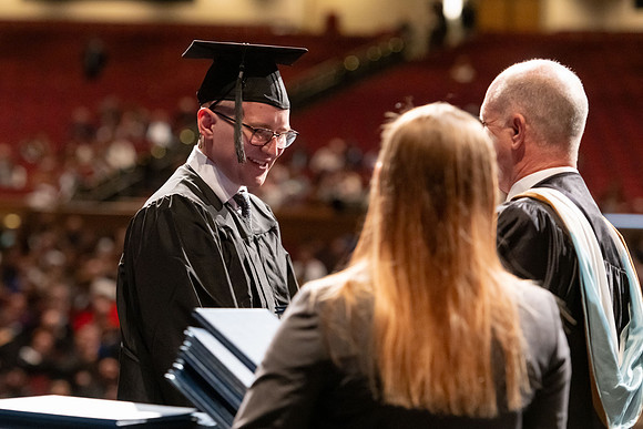 Graduates walk across the stage and accept their diploma.