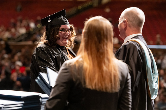 Graduates walk across the stage and accept their diploma.
