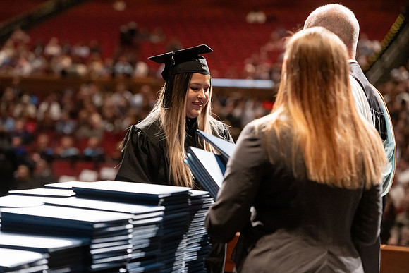Graduates walk across the stage and accept their diploma.