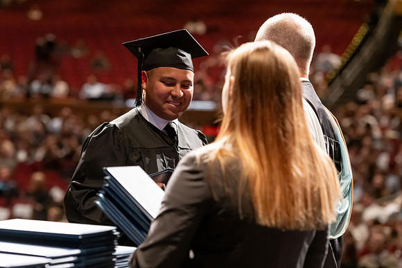 Graduates walk across the stage and accept their diploma.