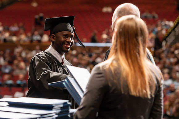 Graduates walk across the stage and accept their diploma.