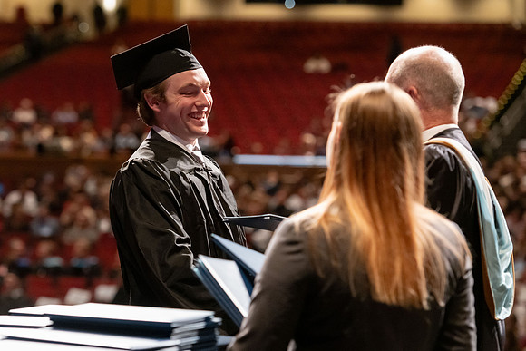 Graduates walk across the stage and accept their diploma.