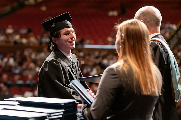 Graduates walk across the stage and accept their diploma.