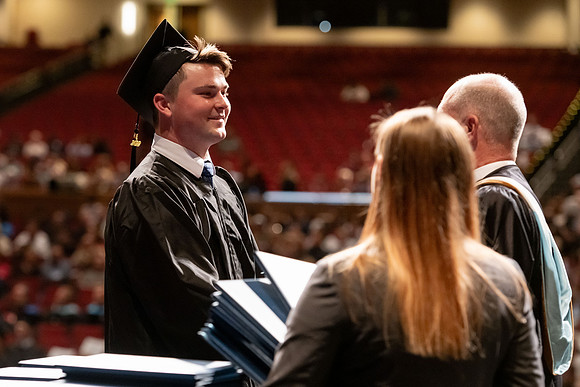 Graduates walk across the stage and accept their diploma.