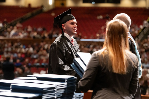 Graduates walk across the stage and accept their diploma.