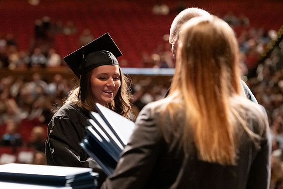 Graduates walk across the stage and accept their diploma.