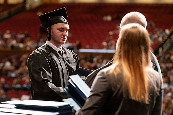 Graduates walk across the stage and accept their diploma.