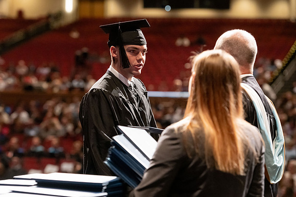 Graduates walk across the stage and accept their diploma.