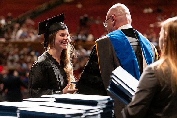 Graduates walk across the stage and accept their diploma.