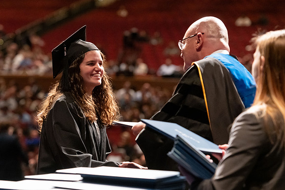 Graduates walk across the stage and accept their diploma.